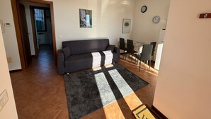 A living room with a sofa, a dining table with chairs, a rug, and a hallway leading to another room. - House at the Knoll (Montescano)