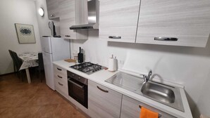 A compact kitchen with a gas stove, oven, sink, and a dining area with a table and chairs. - House at the Knoll (Montescano)