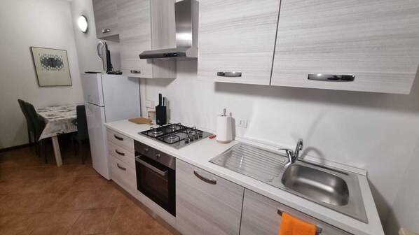 A compact kitchen with a gas stove, oven, sink, and a dining area with a table and chairs. - House on the Hill (Montescano)