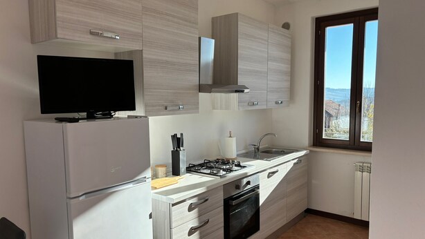 A modern kitchen with a built-in gas stove, oven, and a flat-screen TV on a white cabinet. - House at the Knoll (Montescano)