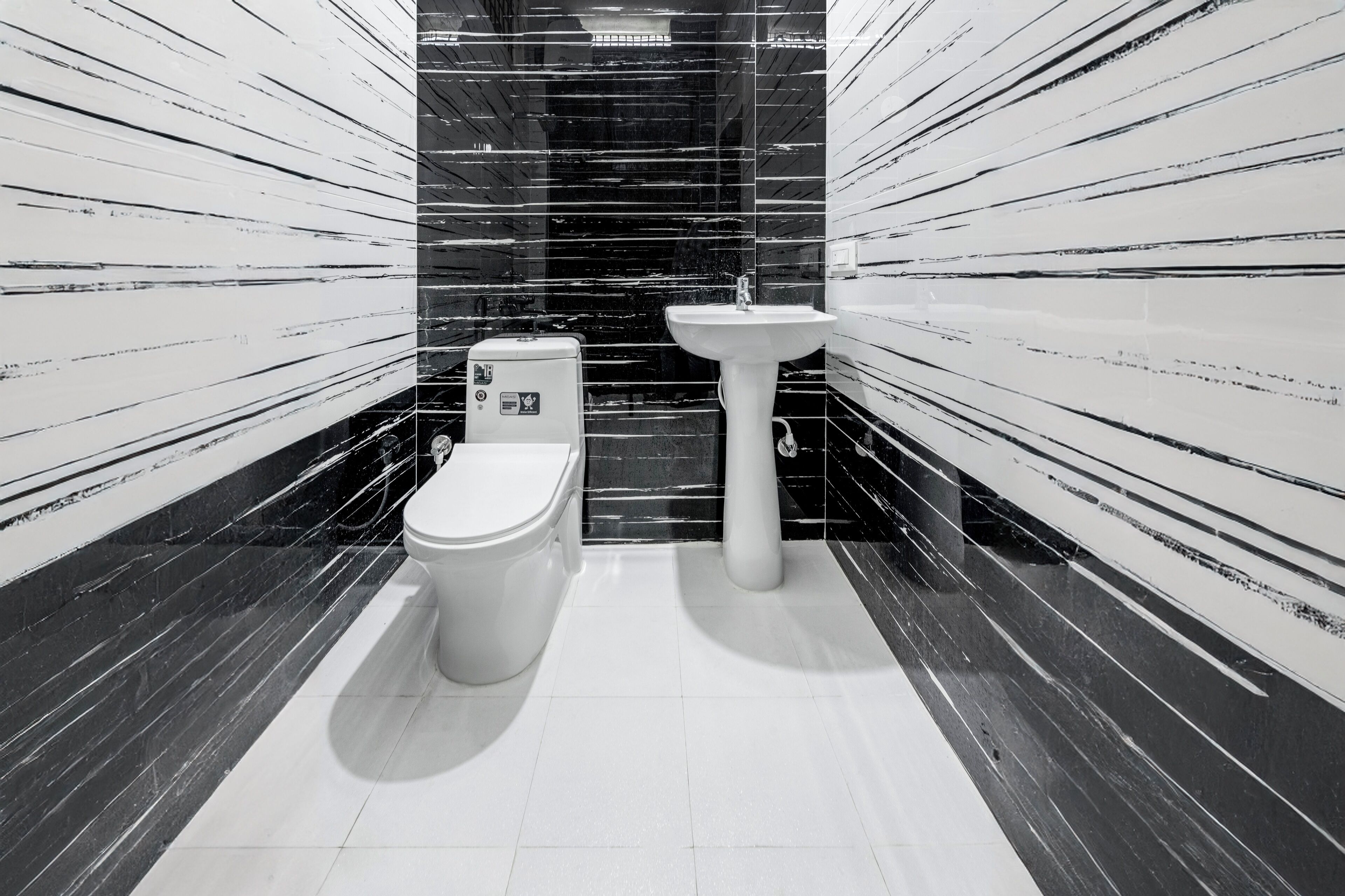 A modern bathroom with a toilet and sink, black and white striped walls, and a tiled floor.