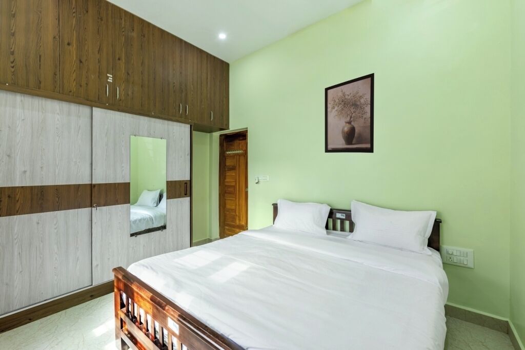 A bedroom with a bed, wooden wardrobe, a mirror, and a framed picture on the wall.