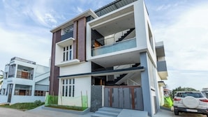 Um edifício residencial moderno de vários andares, com telhado plano, varanda no andar superior e escadaria que leva à entrada.