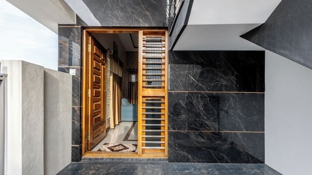 Interior moderno com porta de madeira que dá para um corredor, parede de mármore preto e chão de azulejos.