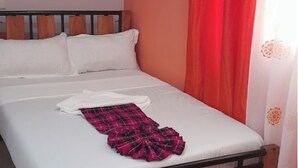 Een bed met witte lakens en een rood-zwart geruit plaid, een houten hoofdbord en een rood gordijn.