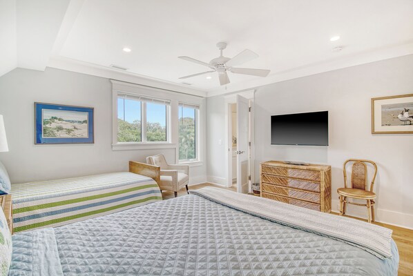 A bedroom with two beds, a ceiling fan, a TV, and a window.