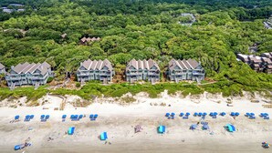 Ein Resort mit mehreren Villen direkt am Strand, einem Sandstrand mit Sonnenschirmen und einem dichten Wald im Hintergrund.