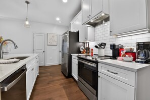 A modern kitchen with white cabinetry, stainless steel appliances, and a wooden floor. - Coastal Tide - Luxury Townhome - Book for Football Season! (Tuscaloosa)
