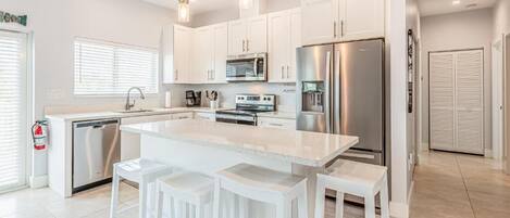 Una cocina moderna con armarios blancos, electrodomésticos de acero inoxidable y una isla central con taburetes de bar.