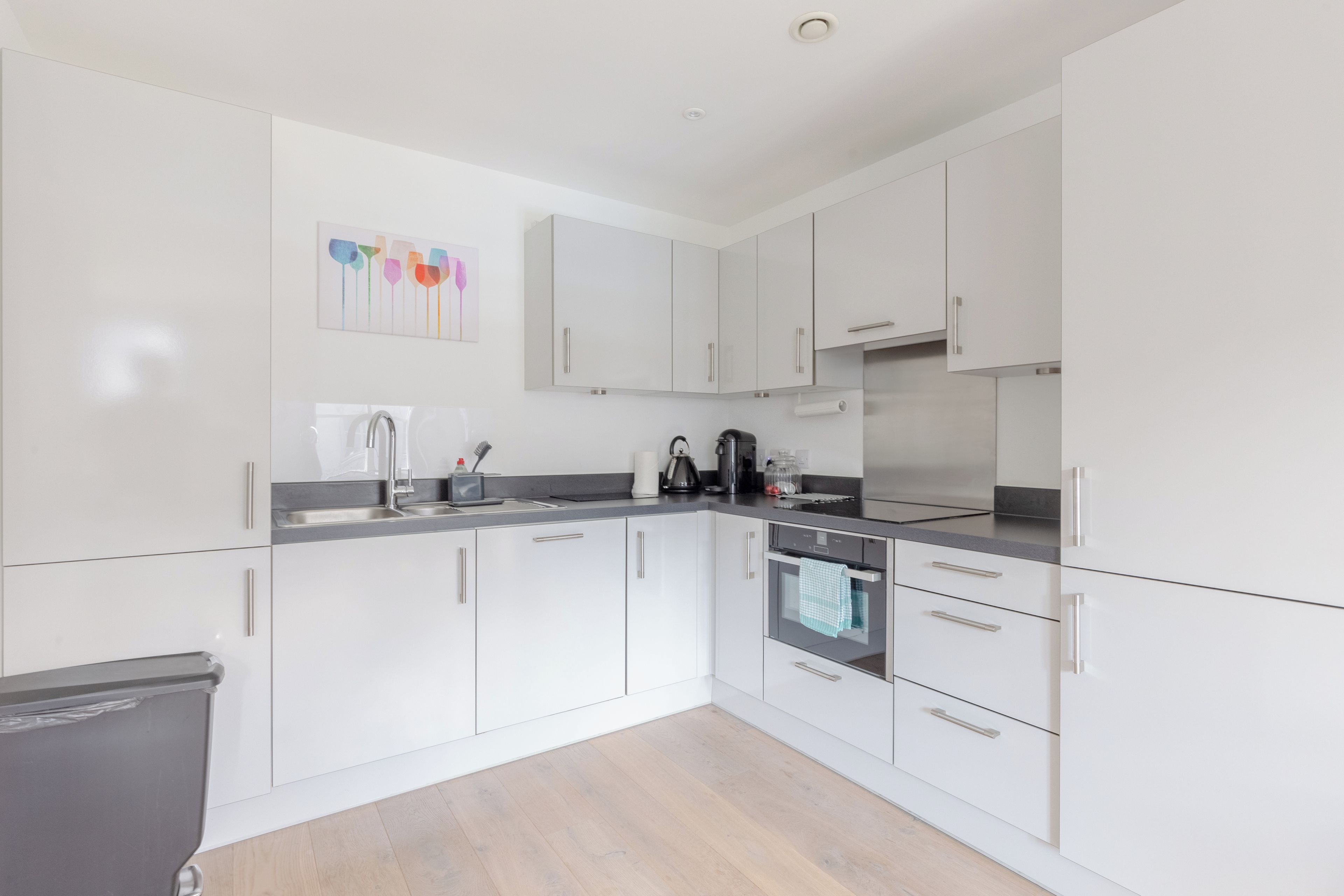 Une cuisine moderne avec des meubles blancs, des appareils en acier inoxydable et un plancher en bois.