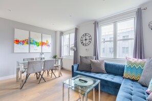 A modern living room with a blue sofa, a glass coffee table, and a dining area with a glass table and chairs. - Chic 1BD Flat in the Heart of Islington! (Greater London)