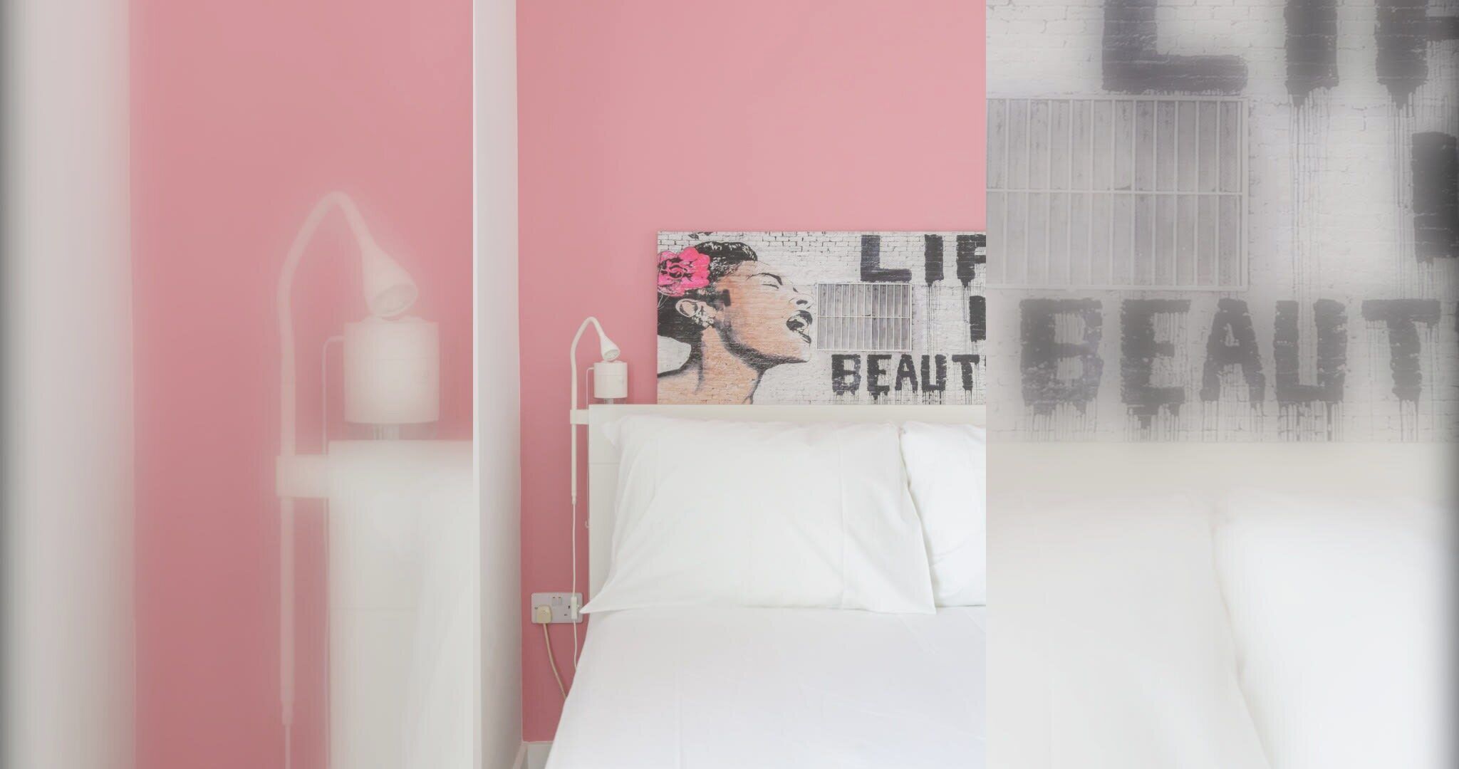 A bedroom with a bed, a wall-mounted light, and a decorative piece with text.