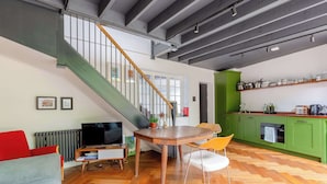 A modern kitchen with green cabinets, a wooden dining table, and a herringbone floor pattern. - Industrial Chic 1BD Stable Conversion, Kings Cross (London)