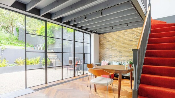 A modern interior with a herringbone wood floor, a brick wall, a large window, and a red carpeted staircase. - Industrial Chic 1BD Stable Conversion, Kings Cross (London)