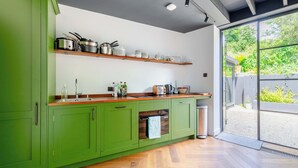 A modern kitchen with green cabinets, wooden countertops, and a built-in oven. - Industrial Chic 1BD Stable Conversion, Kings Cross (London)