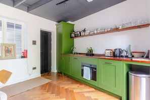 A modern kitchen with green cabinets, a wooden countertop, and a variety of kitchen appliances.