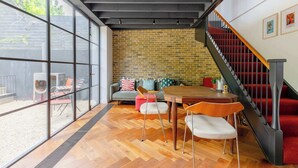 A modern interior with a brick wall, a staircase with red steps, and a dining area with chairs and a table. - Industrial Chic 1BD Stable Conversion, Kings Cross (London)