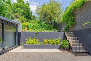 Ein moderner Außenbereich mit einer Betonstiege, die zu einer Terrasse führt, umgeben von Grünpflanzen und einem Holzzaun.