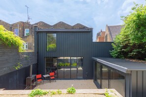 A modern house with a large glass door leading to a patio area with outdoor seating.