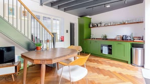 A modern kitchen with green cabinets, a wooden dining table, and a herringbone floor pattern. - Industrial Chic 1BD Stable Conversion, Kings Cross (London)