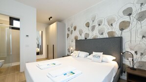Une chambre d’hôtel moderne avec un grand lit, une table de chevet, une petite table et un mur orné d’un motif floral.
