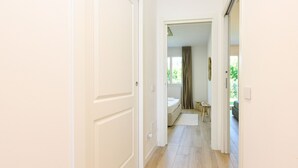 Un pasillo con piso de madera que conduce a un dormitorio con cama, ventana y cortina.