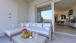 Una sala de estar moderna con un sofá blanco, una mesa de centro con frutas y champán, y vistas a una zona de comedor a través de una puerta abierta.
