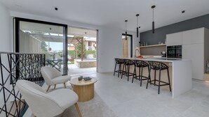 A modern kitchen with a bar area, white cabinetry, and a large sliding glass door leading to an outdoor patio. - MGH Luxury - Corte Garden Bardolino 34 (Bardolino)