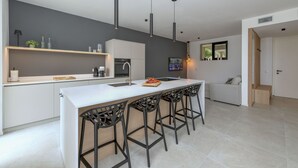 A modern kitchen with a central island, bar stools, pendant lighting, and a built-in oven. - MGH Luxury - Corte Garden Bardolino 34 (Bardolino)