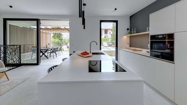 A modern kitchen with a central island, built-in oven, and a dining area with outdoor seating. - MGH Luxury - Corte Garden Bardolino 34 (Bardolino)