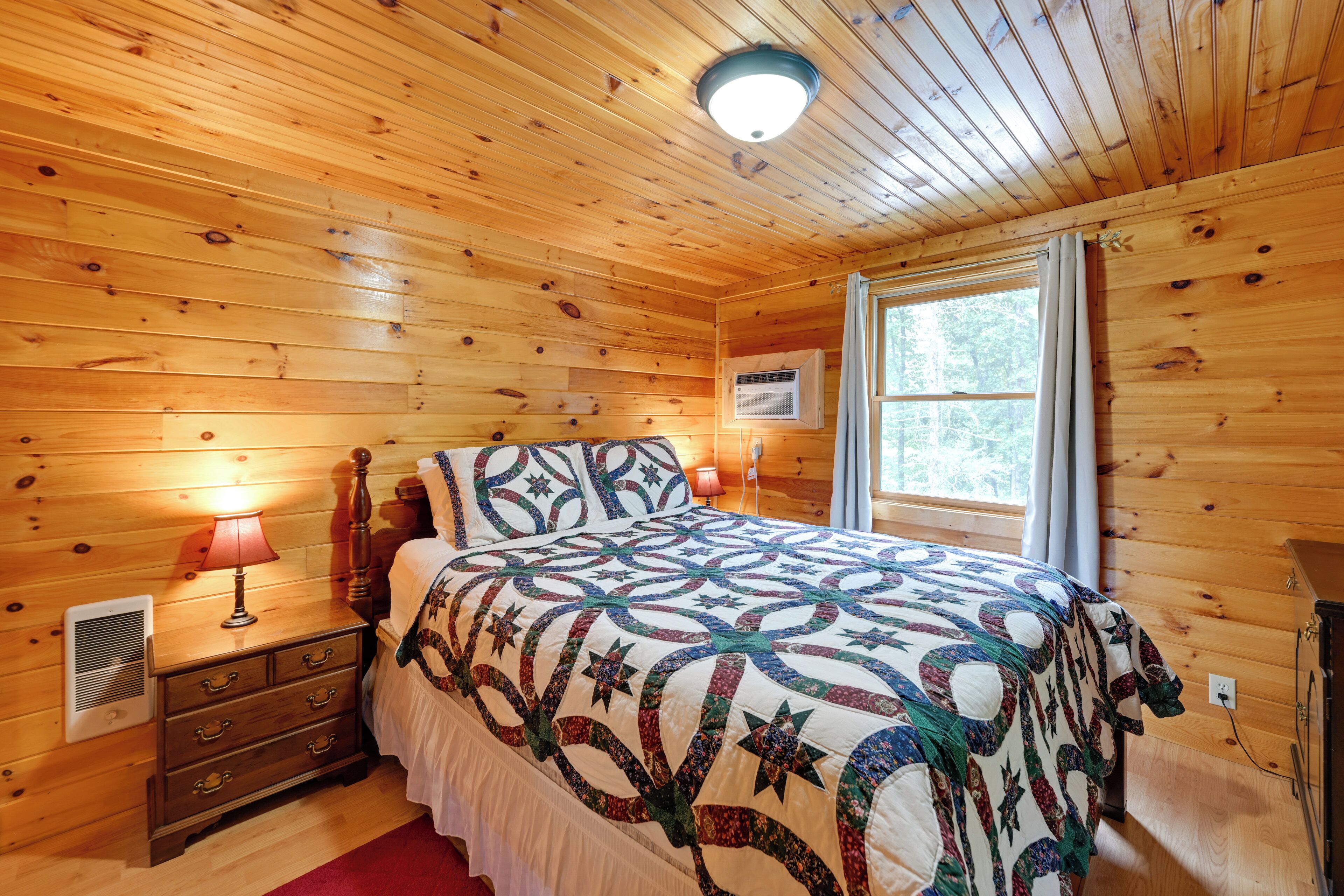Un dormitorio con paneles de madera, una cama, una mesita de noche, una lámpara y una ventana con cortinas.
