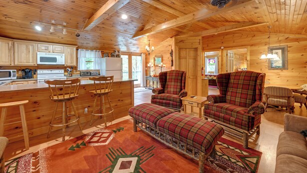 L’intérieur d’un chalet en bois comprend une cuisine, un coin bar, des fauteuils à carreaux et un canapé.