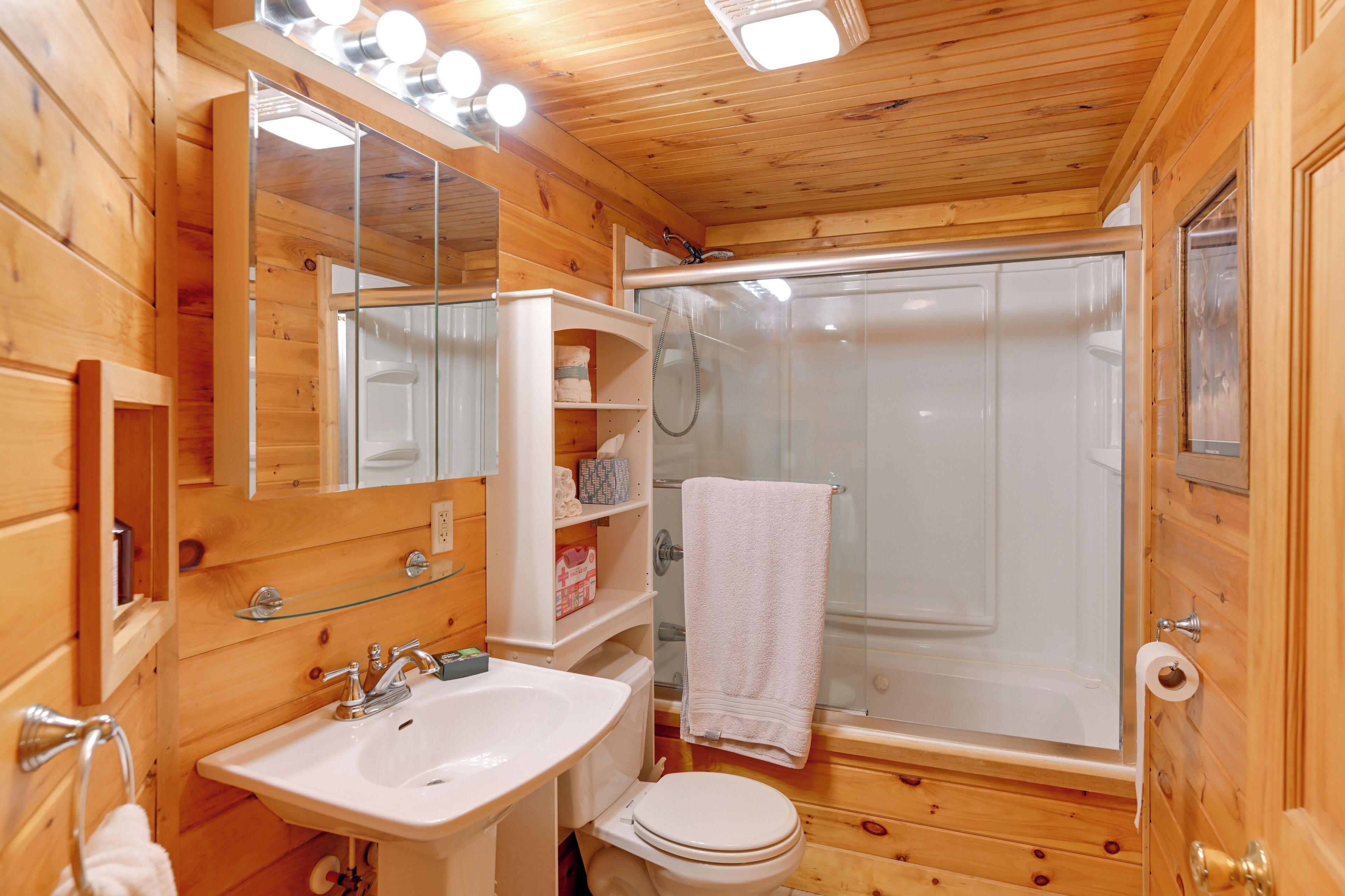 Une salle de bain rustique, aménagée dans une cabane en bois, avec un lavabo, des toilettes et une douche à parois en verre.
