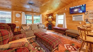 Un intérieur chaleureux de chalet en bois, avec une cheminée, des meubles à motifs écossais et un téléviseur fixé au mur.
