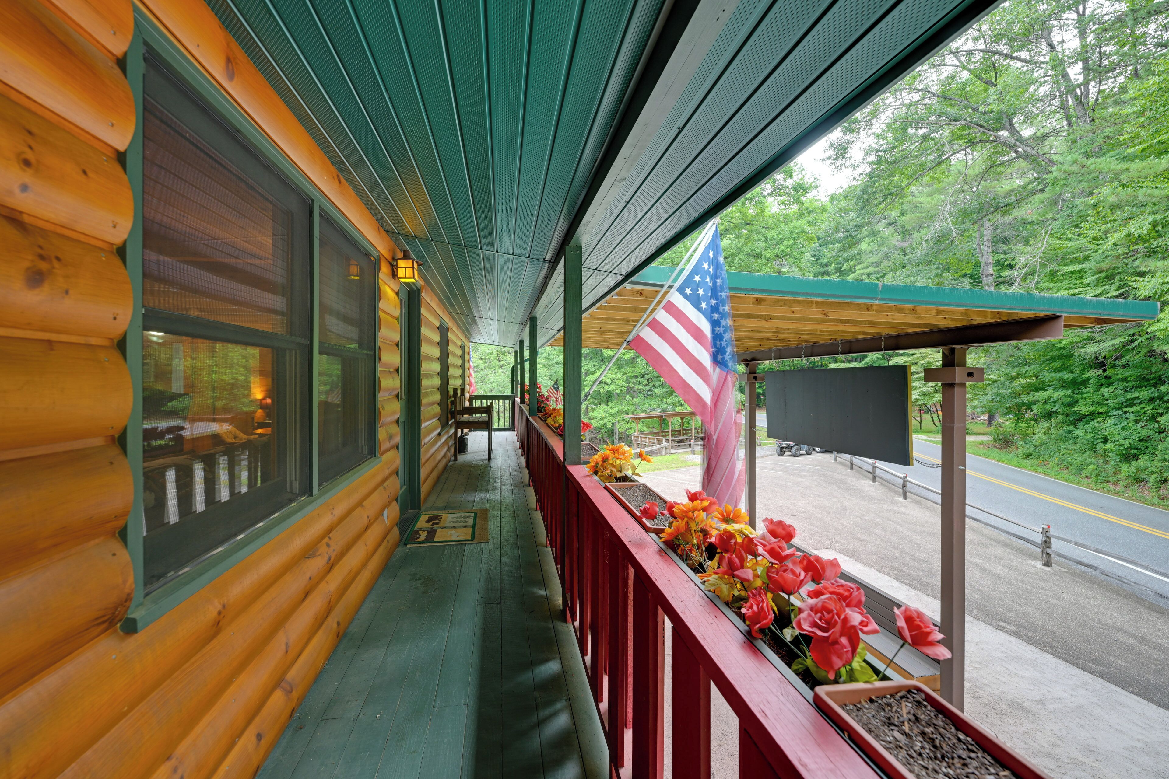 A wooden cabin with a covered porch, a flag, and a view of the road.
