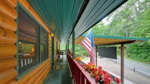 Une cabane en bois avec un porche couvert, un drapeau et une vue sur la route.