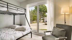 A bedroom with a bunk bed, a chair, a lamp, and a view of the outdoors. - Mashpee Cottage w/ Deck: 6 Mi to South Cape Beach! (Mashpee)