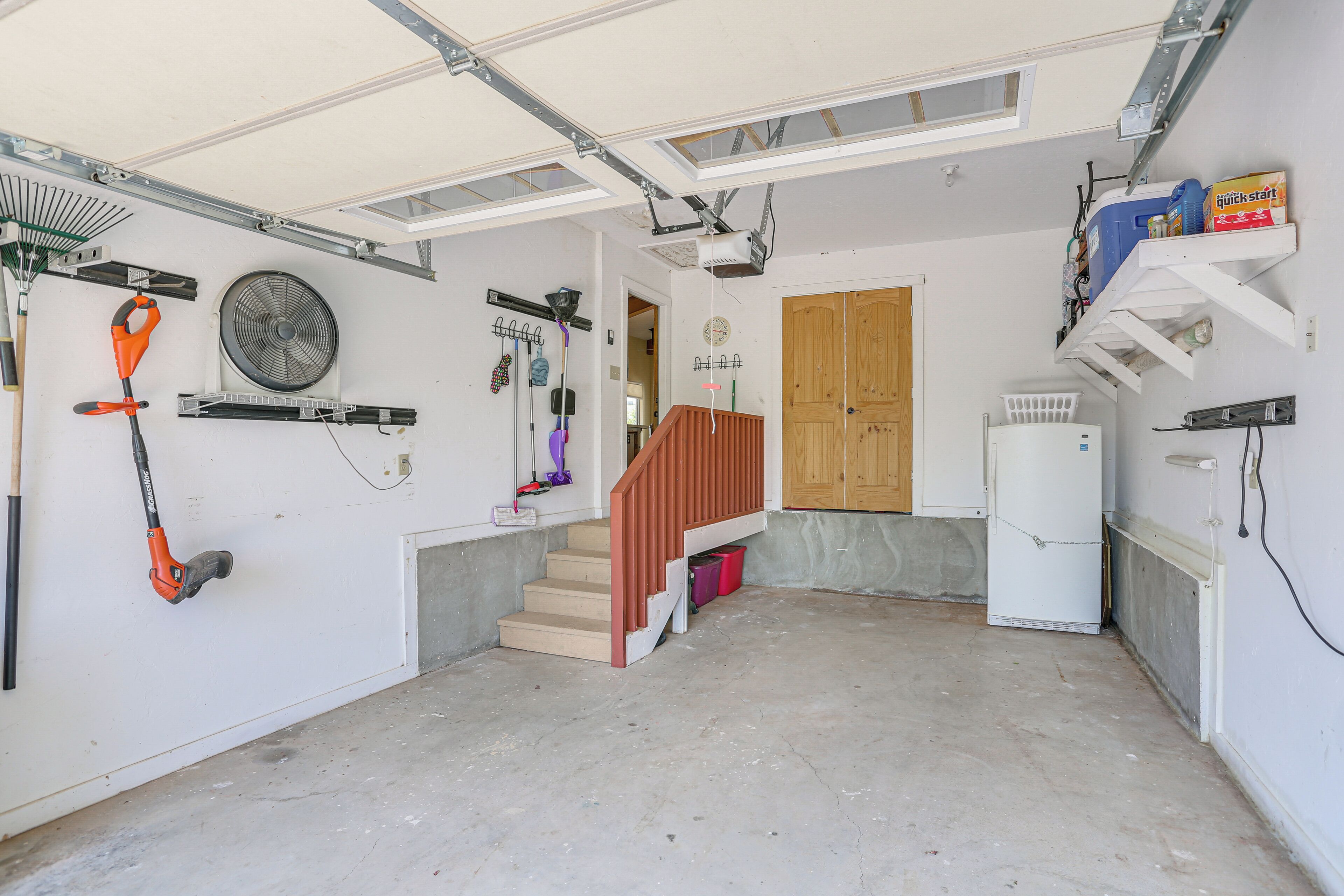 Un garage doté d’un sol en béton, d’une porte en bois et de divers outils et équipements fixés aux murs.