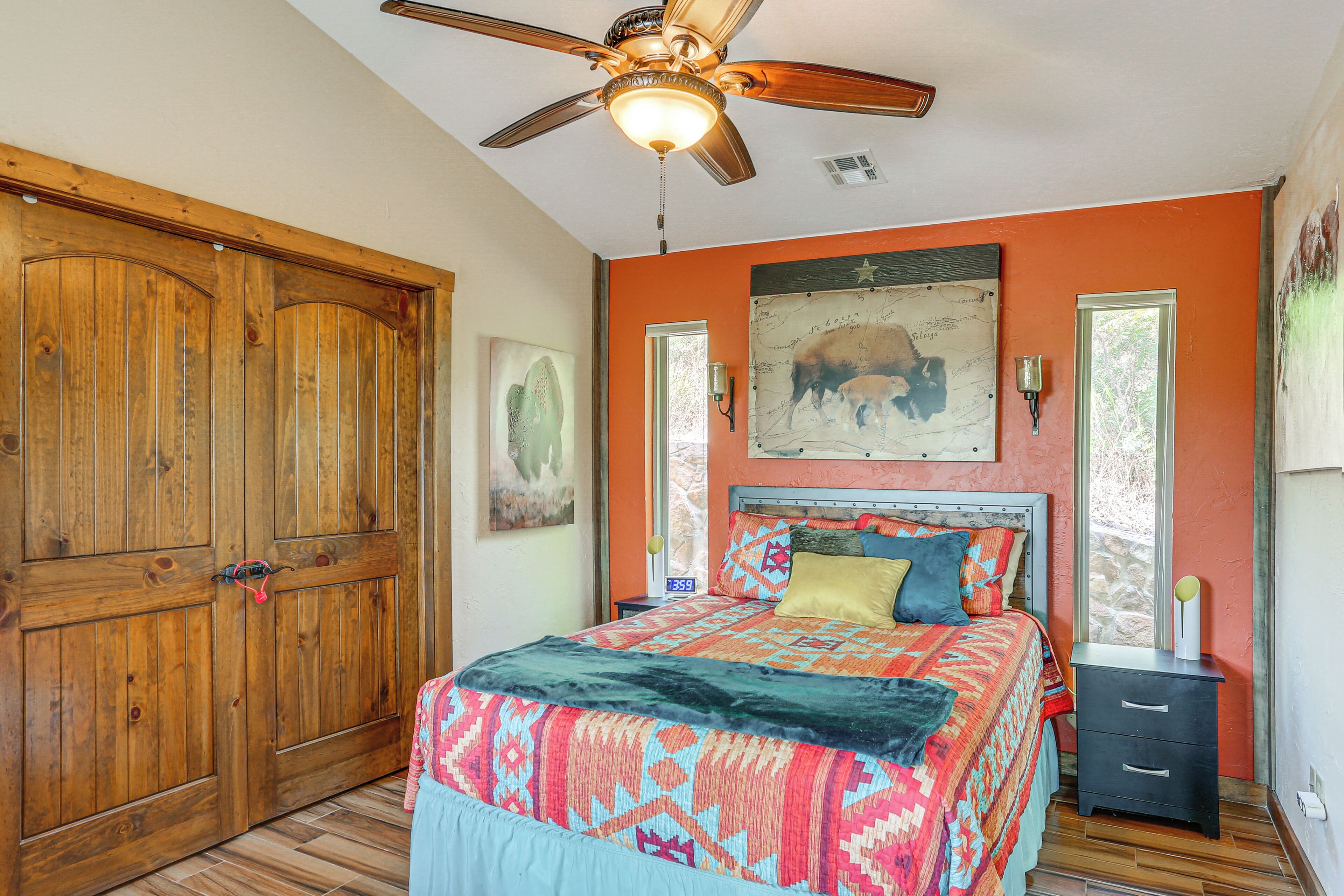 A bedroom with a wooden wardrobe, a bed with patterned bedding, a ceiling fan, and artwork on the walls.
