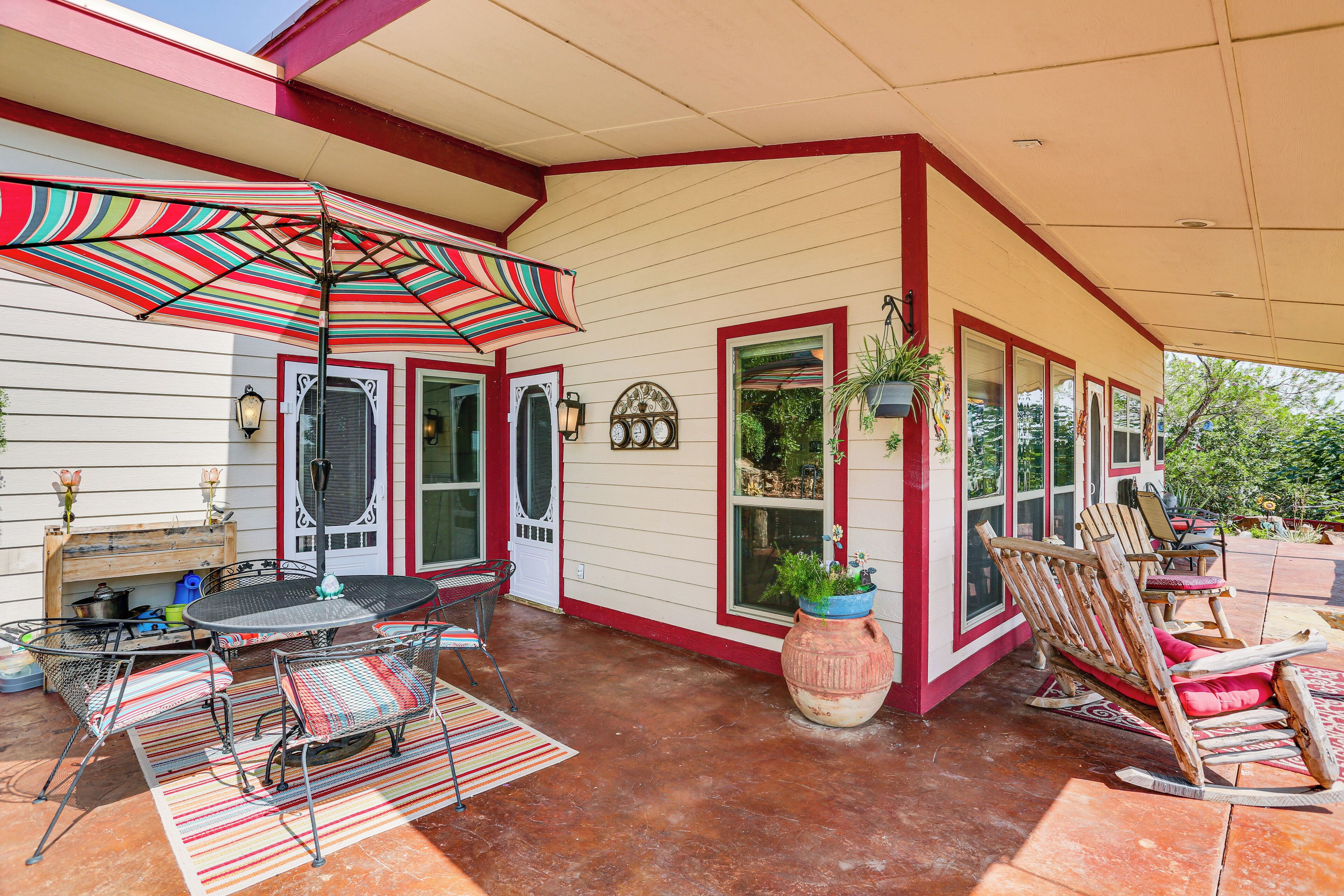 An outdoor patio with a striped umbrella, a metal table and chairs, a rocking chair, and a large potted plant.