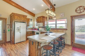 Una cocina con armarios de madera, una isla central con taburetes, un refrigerador, un microondas y una lámpara colgante.