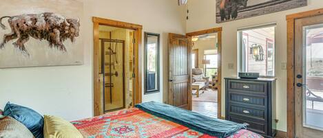 A bedroom with a large bed, a ceiling fan, a door leading to another room, and a painting of a bull on the wall.