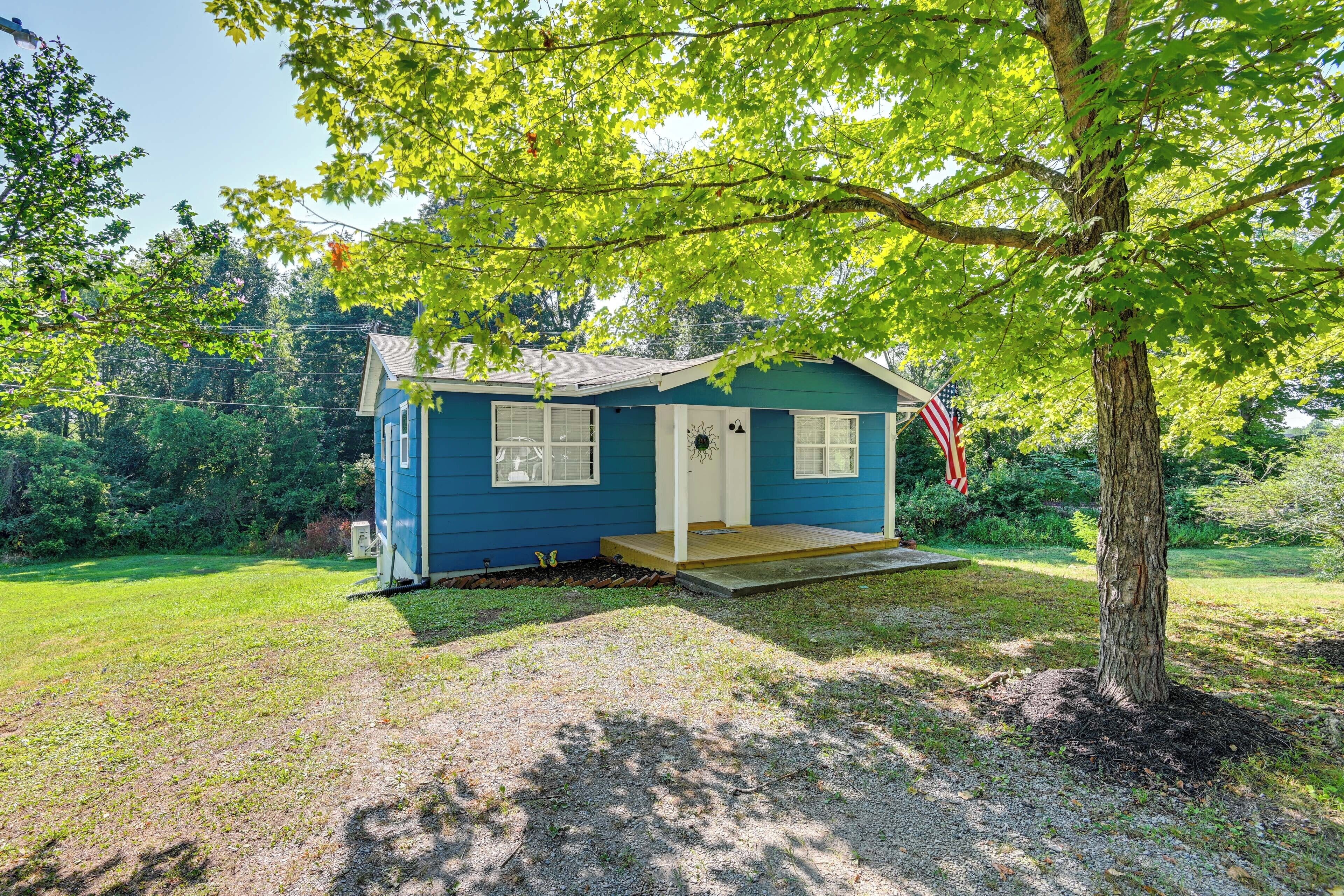 Une petite maison bleue avec un porche, entourée d’arbres et d’herbe.