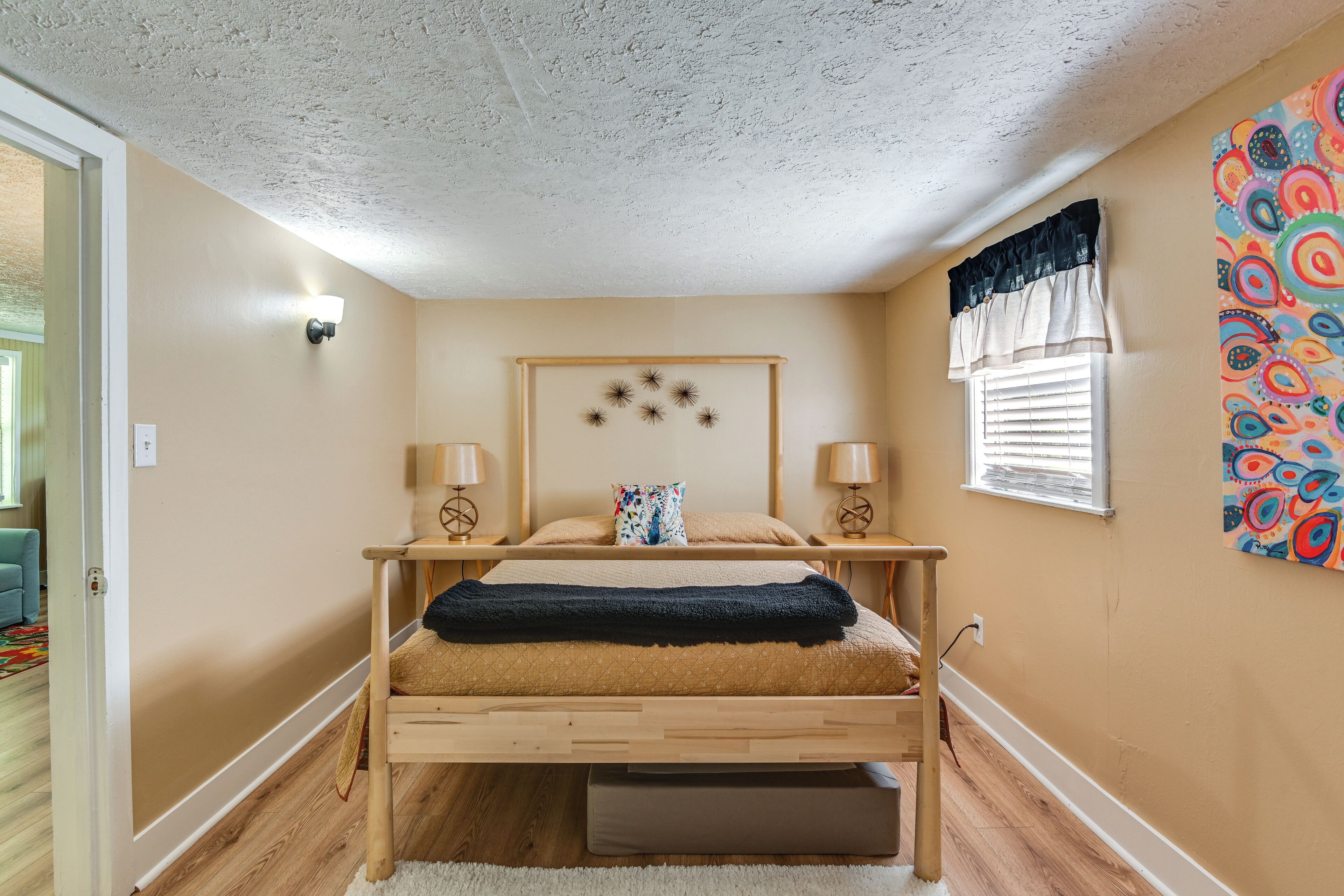 A bedroom with a bed, bedside lamps, a decorative wall piece, and a window with blinds.