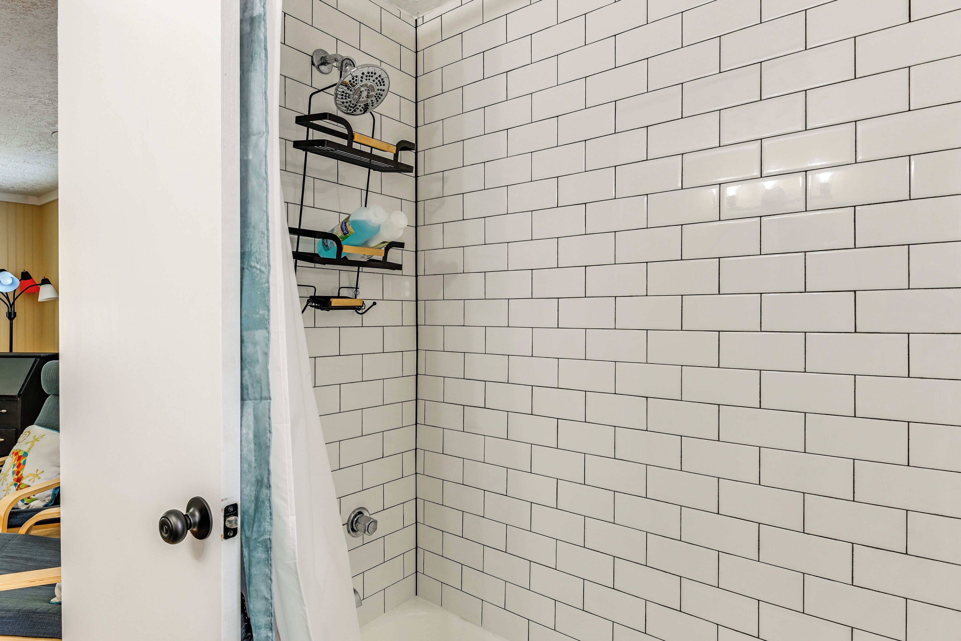 Une douche d’angle avec des carreaux de céramique blancs rectangulaires, un porte-serviettes noir et un pommeau de douche.