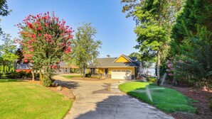 A residential house with a driveway leading to a garage, surrounded by well-maintained lawns and flowering trees. - Lakefront Gem: Hot Tub, Boat Launch Near Greenwood (Cross Hill)