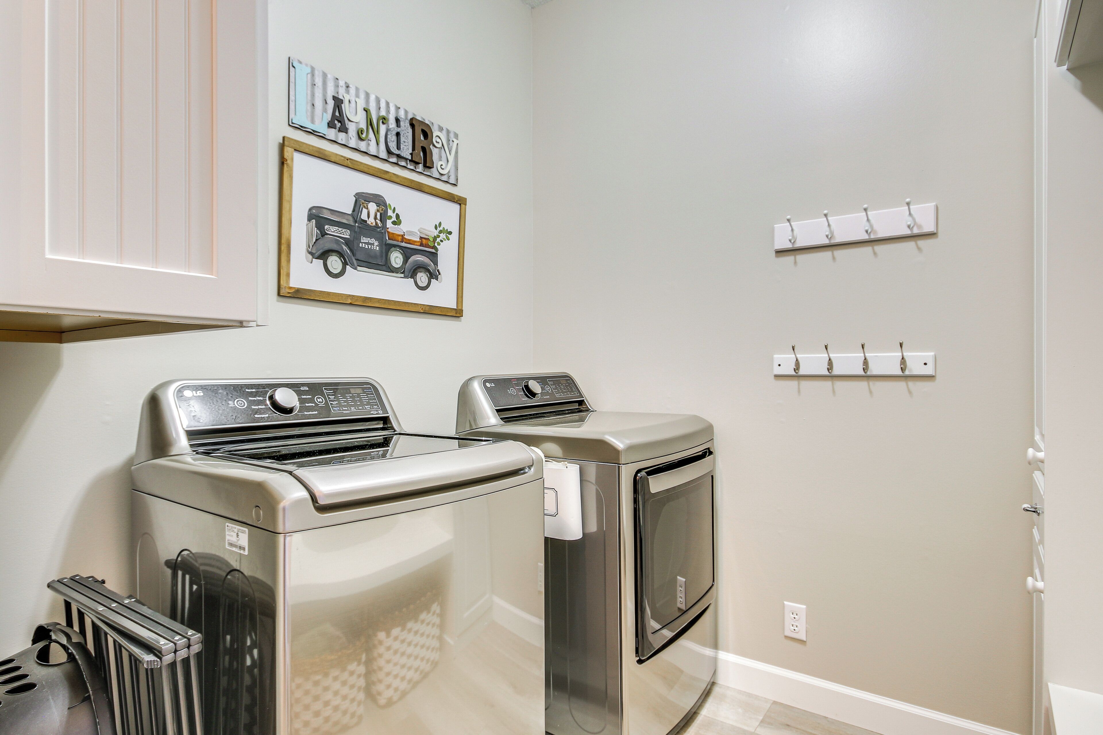 A laundry room with two front-loading washing machines and a dryer, a framed picture of a truck, and a wall-mounted coat rack.