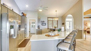 A modern kitchen with stainless steel appliances, a central island with bar stools, and a dining area with a chandelier. - Lakefront Gem: Hot Tub, Boat Launch Near Greenwood (Cross Hill)