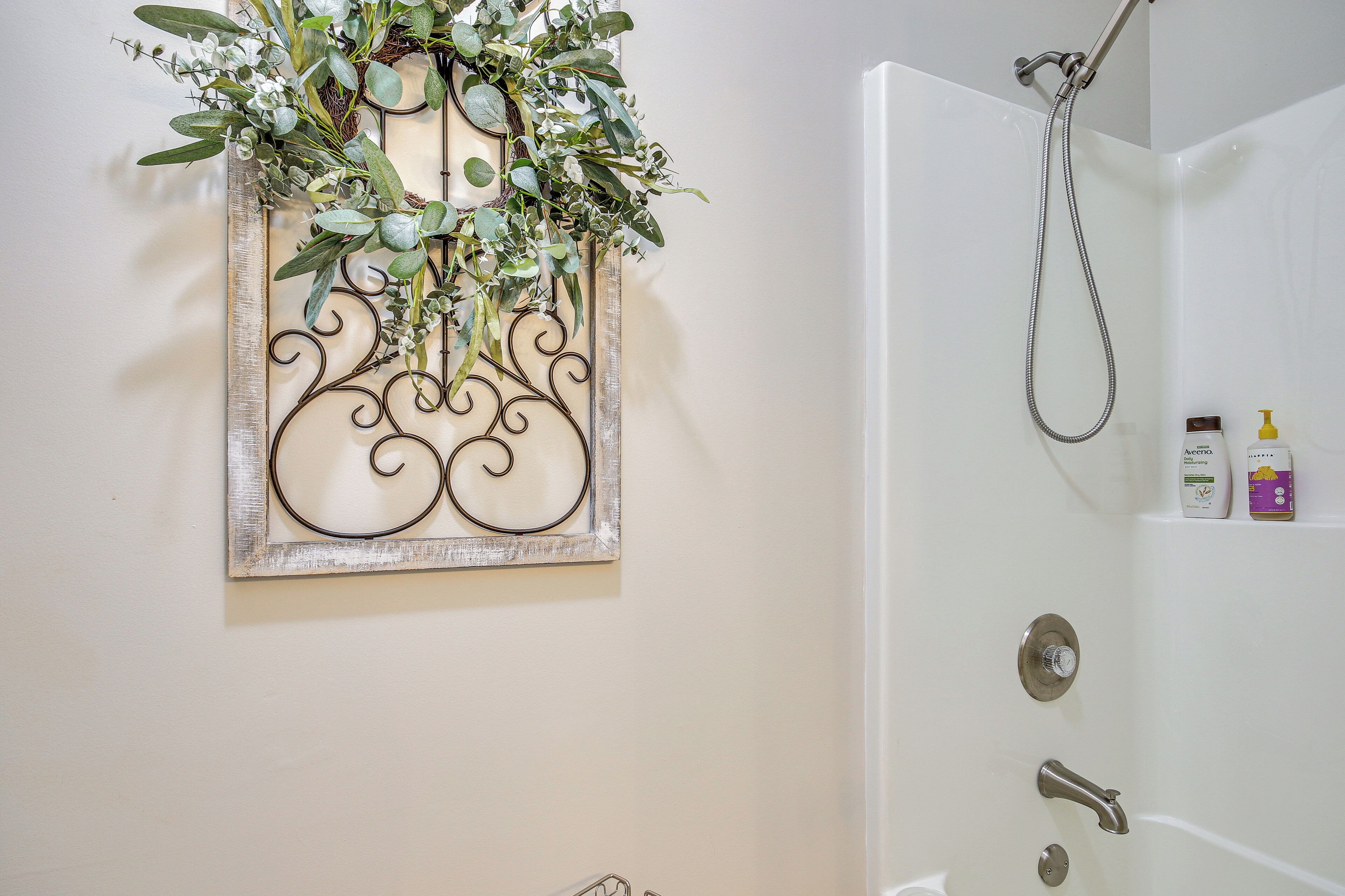 A bathroom with a shower, a decorative wall piece, and toiletries on the shelf.