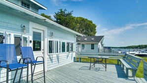 Terraza de madera con sillas azules y una mesa, con vistas a un puerto deportivo lleno de barcos.